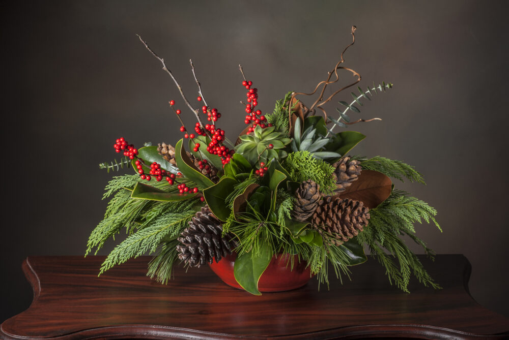 Lush winter holiday arrangement in evergreens and bright red berries with cones and pods delivered.