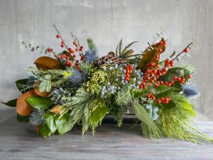 Holiday flower class unique arrangement in long and low style with evergreens, berries, and botanical accents.