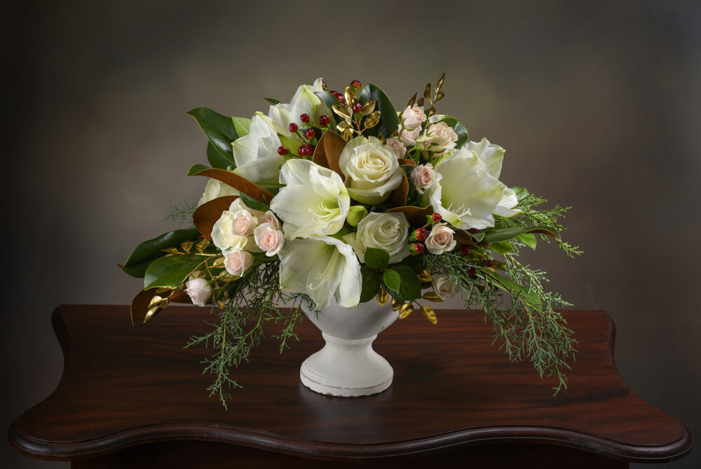 Lush winter white and peach flower arrangement with accents of gold in a white urn