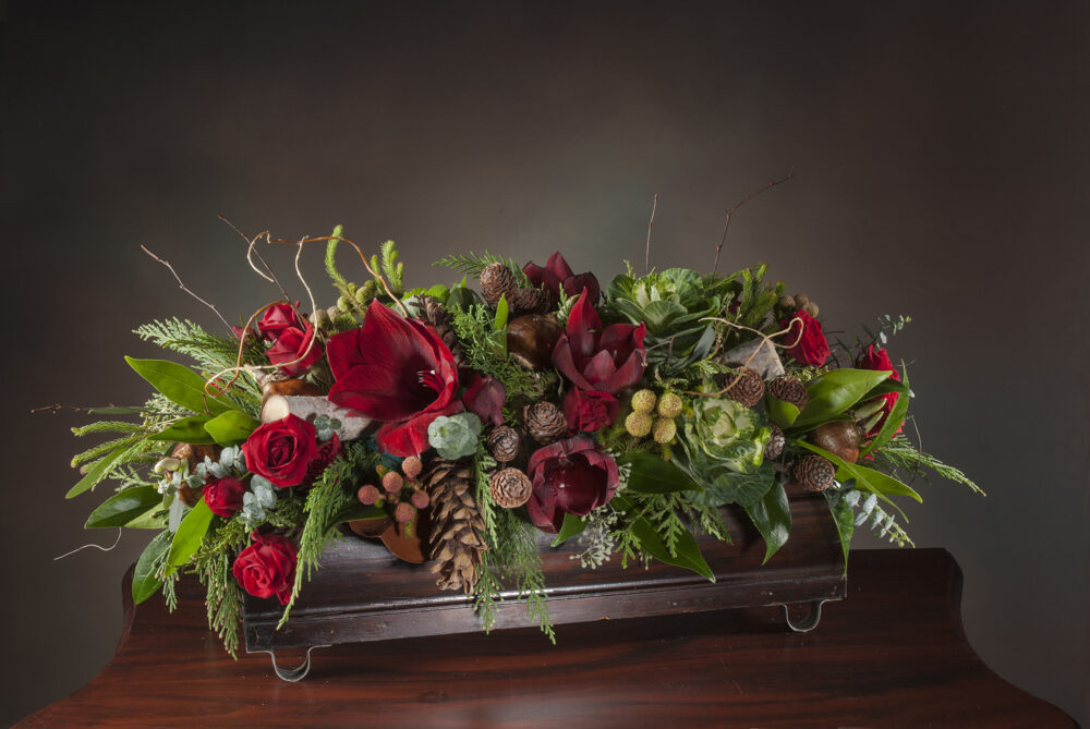Red amaryllis flowers with accents and evergreens in a RWF Original container, holiday centerpiece delivered