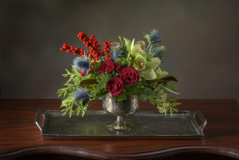 Lovely unique fresh flower arrangement in rich reds, and blue thistle accented with evergreens and berries delivered