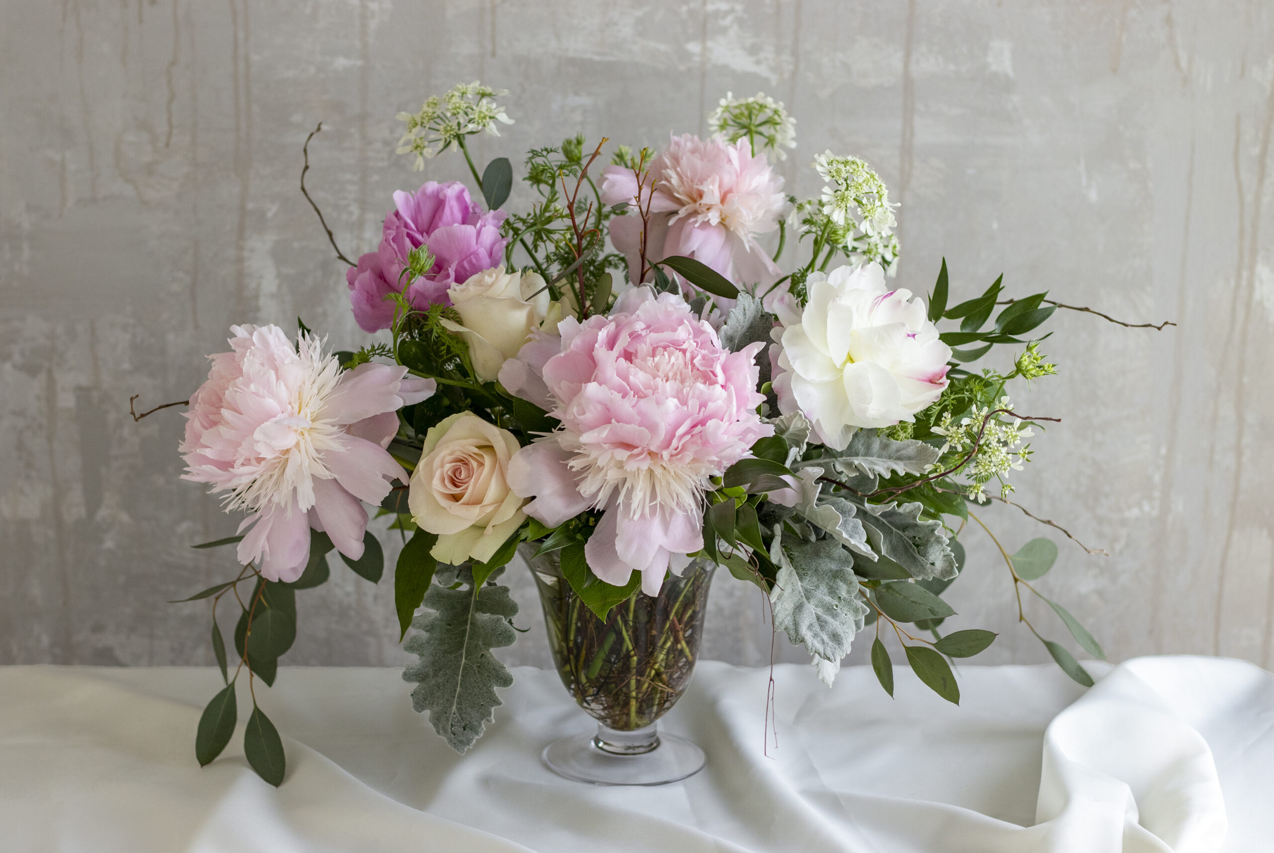 Class flower arrangement with perfect spring peonies and seasonal accent blooms designed in a flared pedestal vase.