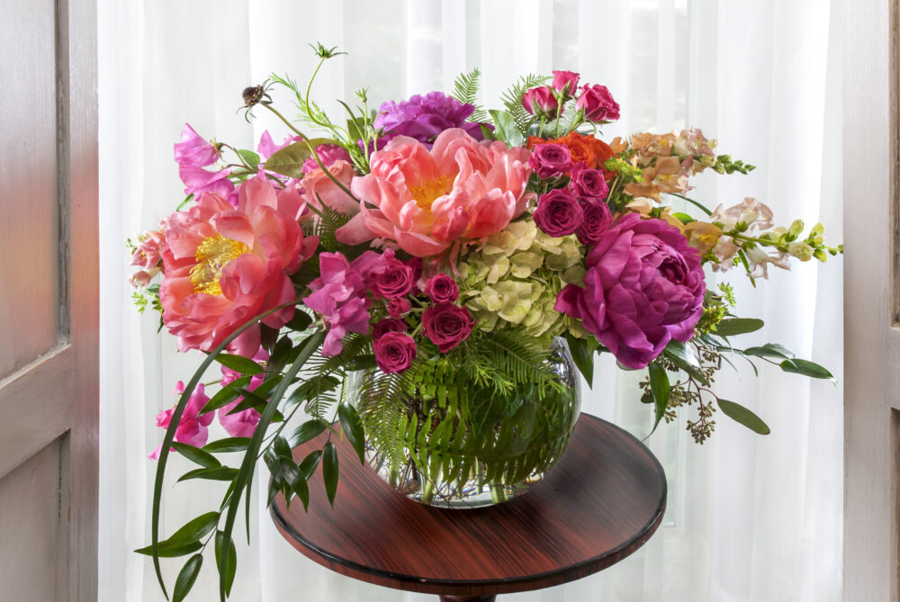 Vibrant, lush peonies in a fresh flower arrangement in bright pink, coral, and apricot spring blooms in an emerald leaf wrap, delivered for you.