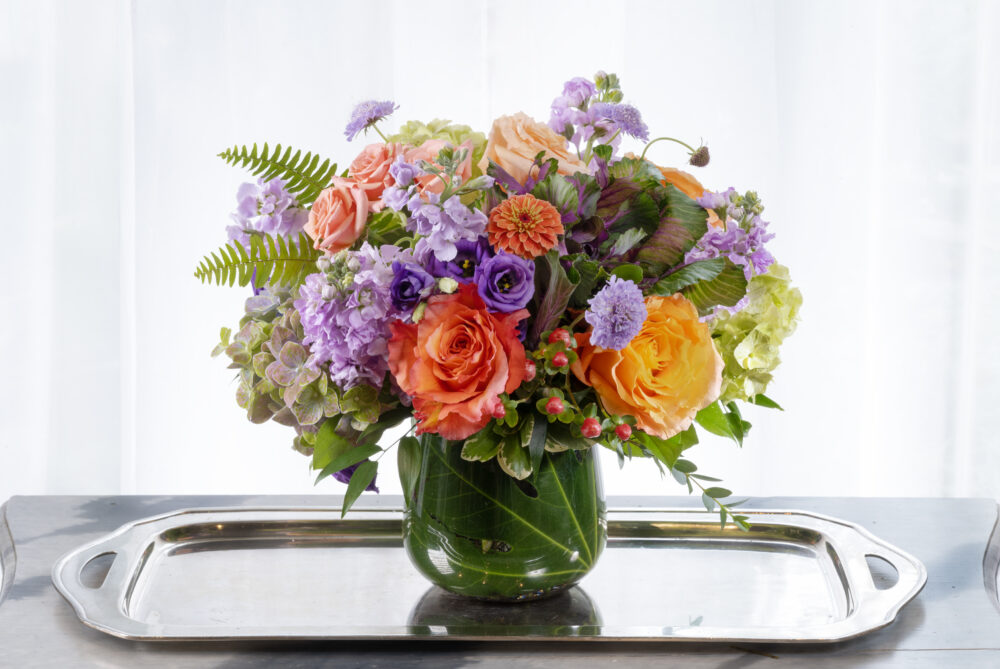A vibrant mix of summer fresh flowers with coral, peach, lavender, and purple in an emerald leaf wrap for a cheerful gift, delivered.