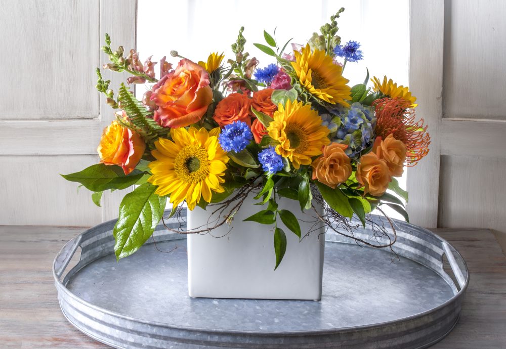 Vibrant and colorful summer fresh flower arrangement with sunflowers and bright blue accents, delivered.
