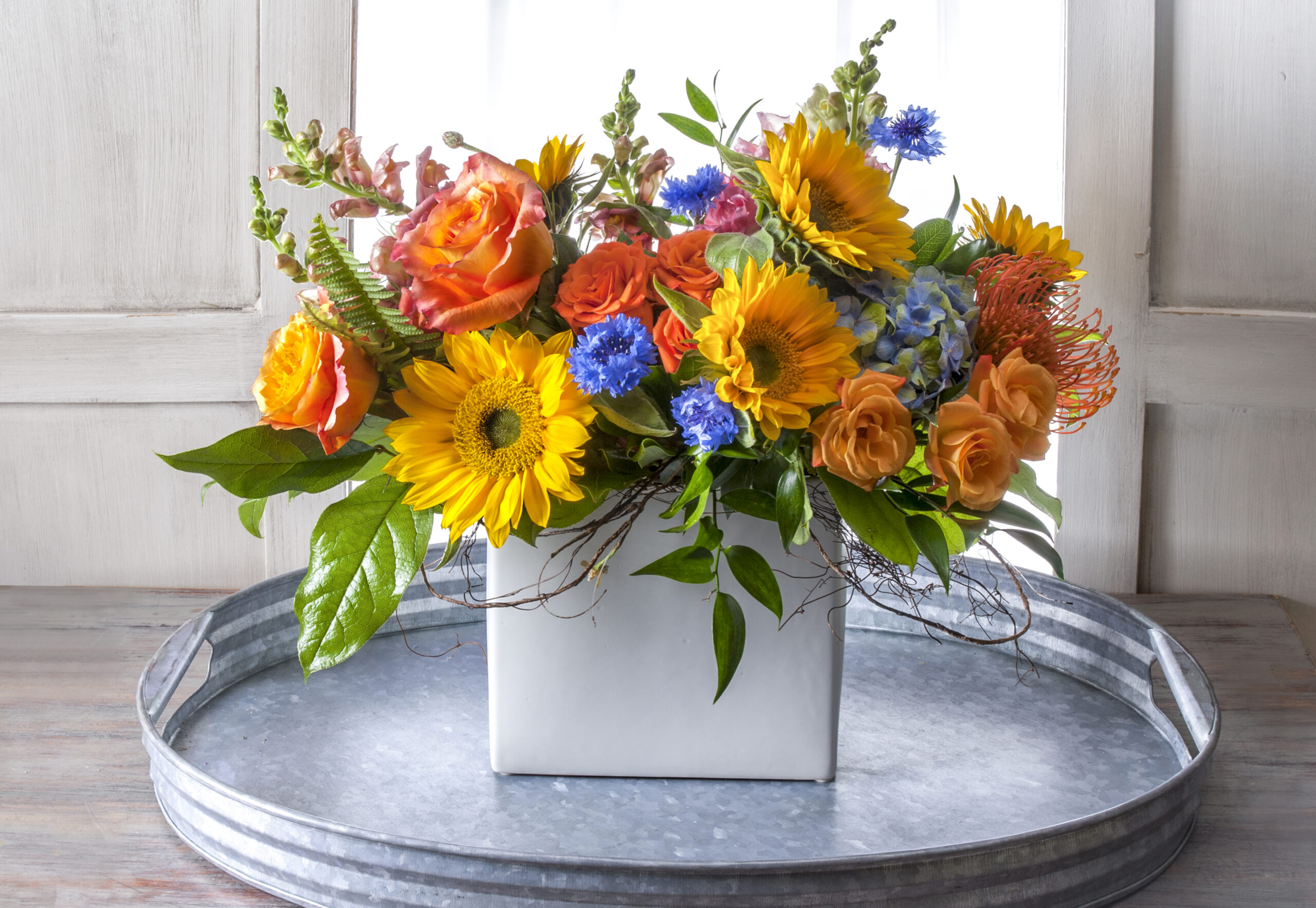 Brighten someone’s day with a vibrant, colorful summer fresh flower arrangement with sunflowers and bright blue accents, delivered for you. Vibrant and colorful summer fresh flower arrangement with sunflowers and bright blue accents, delivered.