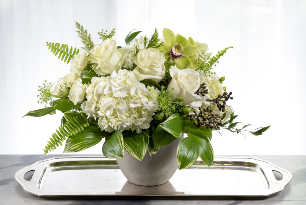 A unique, fresh bright green, and crisp white summer flower arrangement with orchid accents designed in a smooth grey pot.
