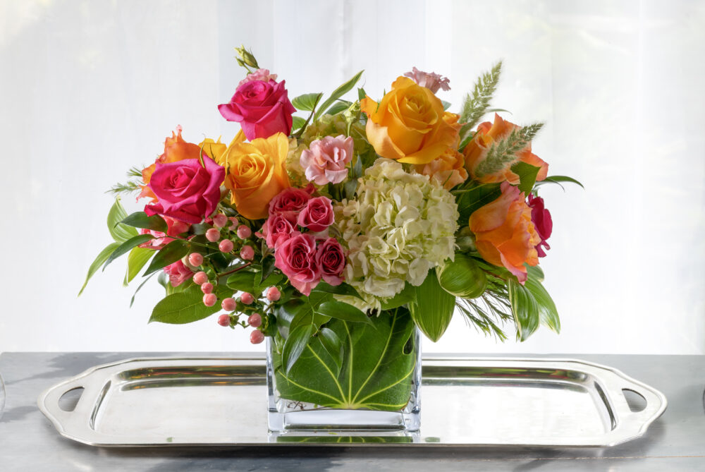 Bold pink and coral colors with summer yellow blooms, a vibrant fresh flower arrangement in an emerald leaf wrap.
