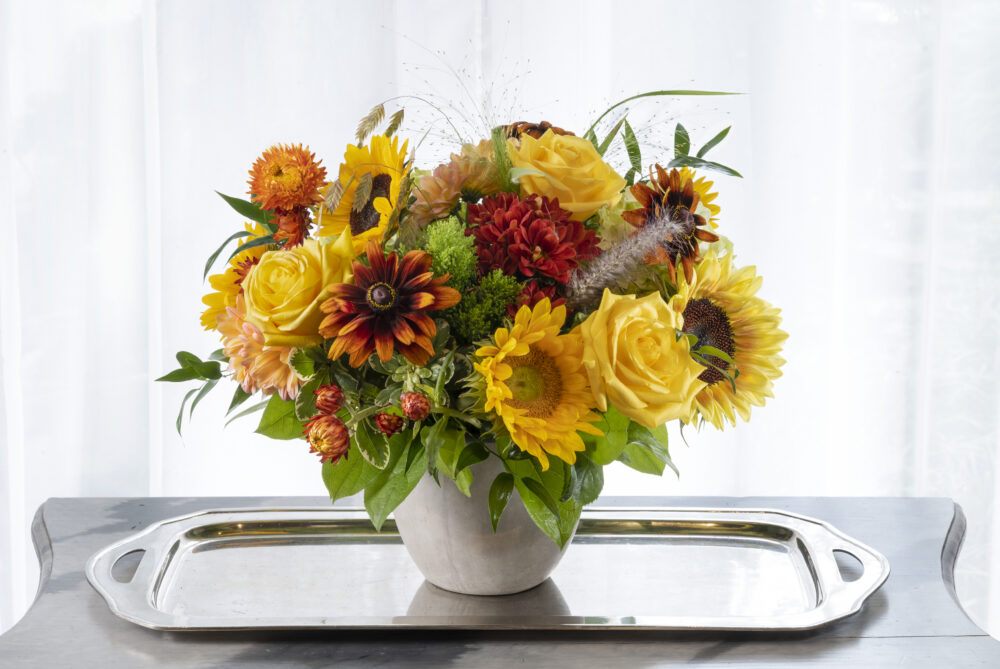 A cheerful gift, bright summer sunflowers with yellow, orange, and rust red fresh flowers in a smooth cement pot, delivered.