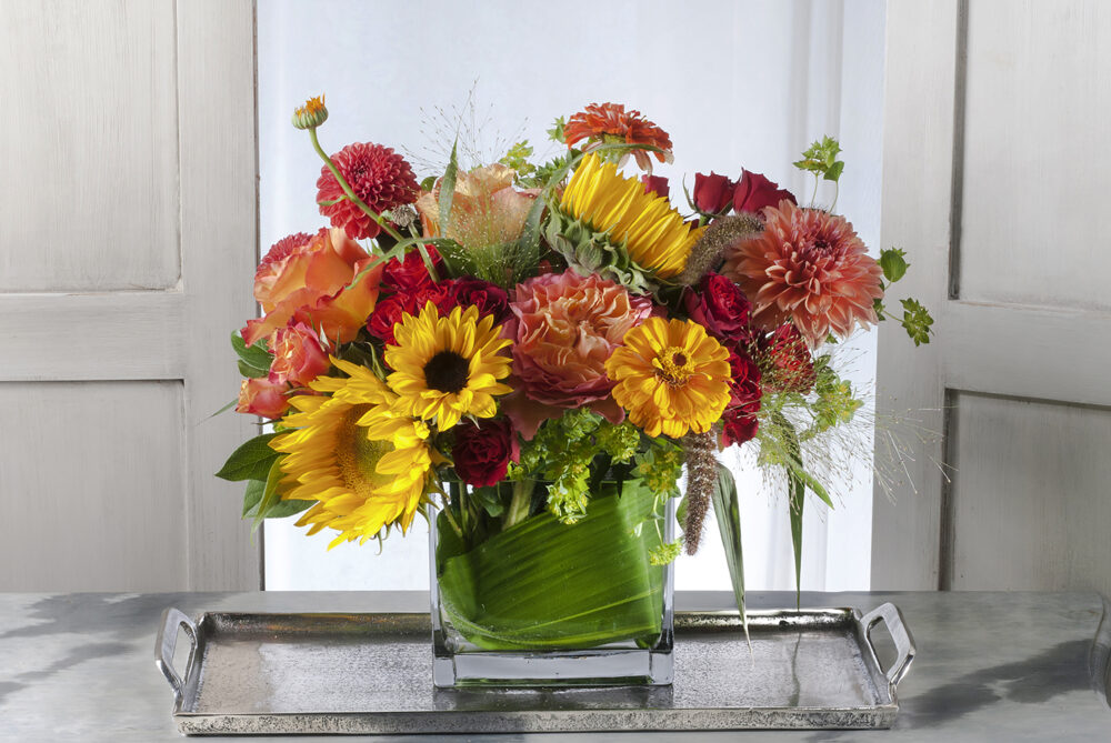 A gift in bright summer colors of yellow, orange, and crimson red flowers wrapped in an emerald leaf, designed in a rectangle, delivered for you.