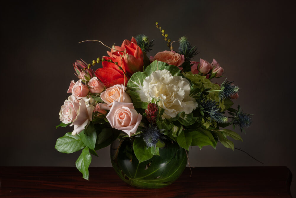 Striking design in pretty colors of orange, peach, green, and soft blue. Designed in a leaf-wrapped rose bowl.