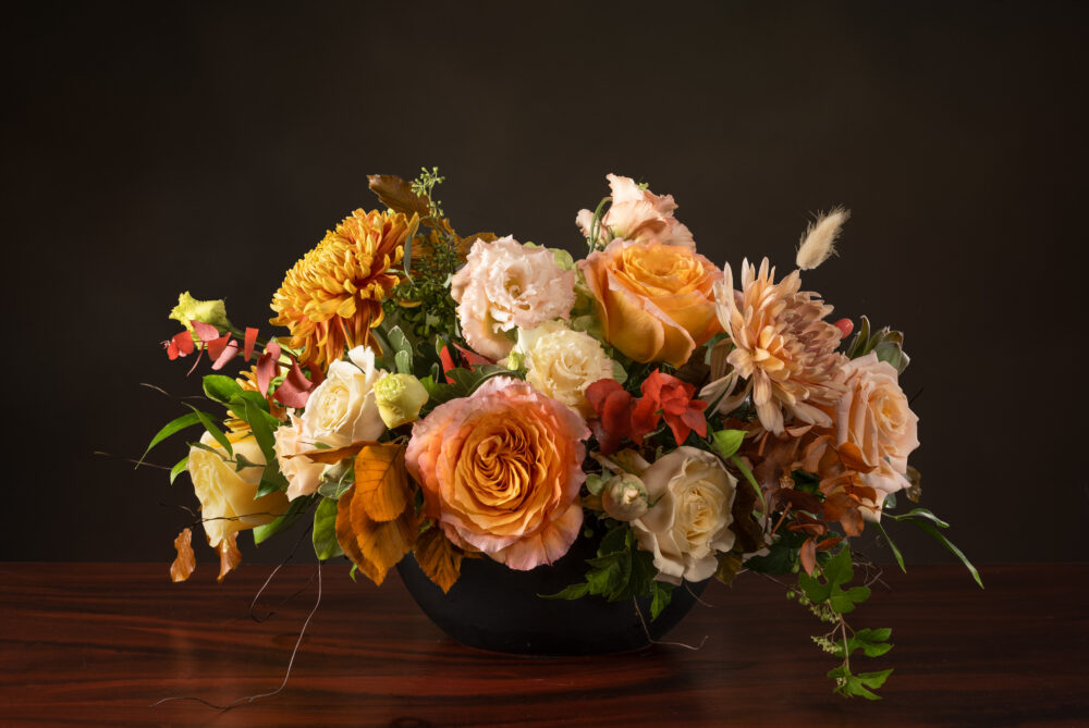 Fresh flower arrangement in soft autumn colors of blush, peach, coral, and amber, designed in a matte black oval, delivered.