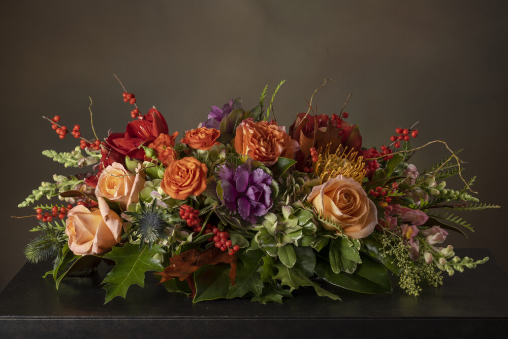 Colorful lush flowers and autumn foliage with berries in colors of orange, amber, and purple in a striking Thanksgiving centerpiece.