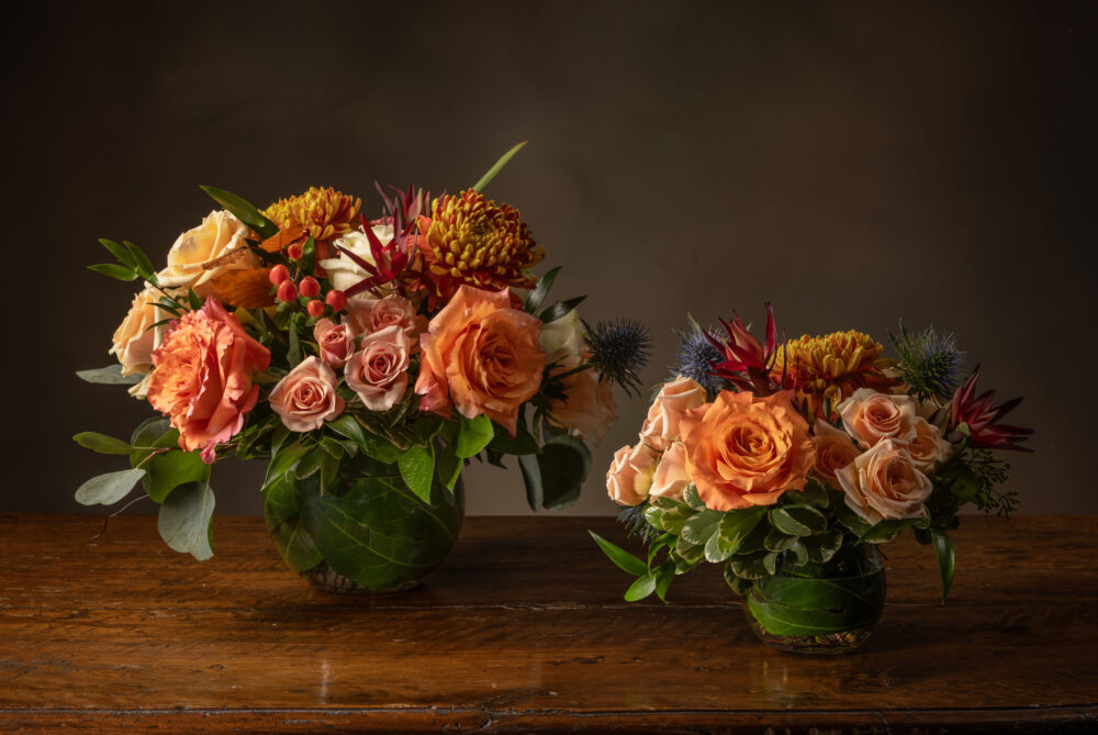 Colorful bright flowers and autumn foliage with berries in orange, amber, and soft blue in a striking trio for a Thanksgiving tablescape.
