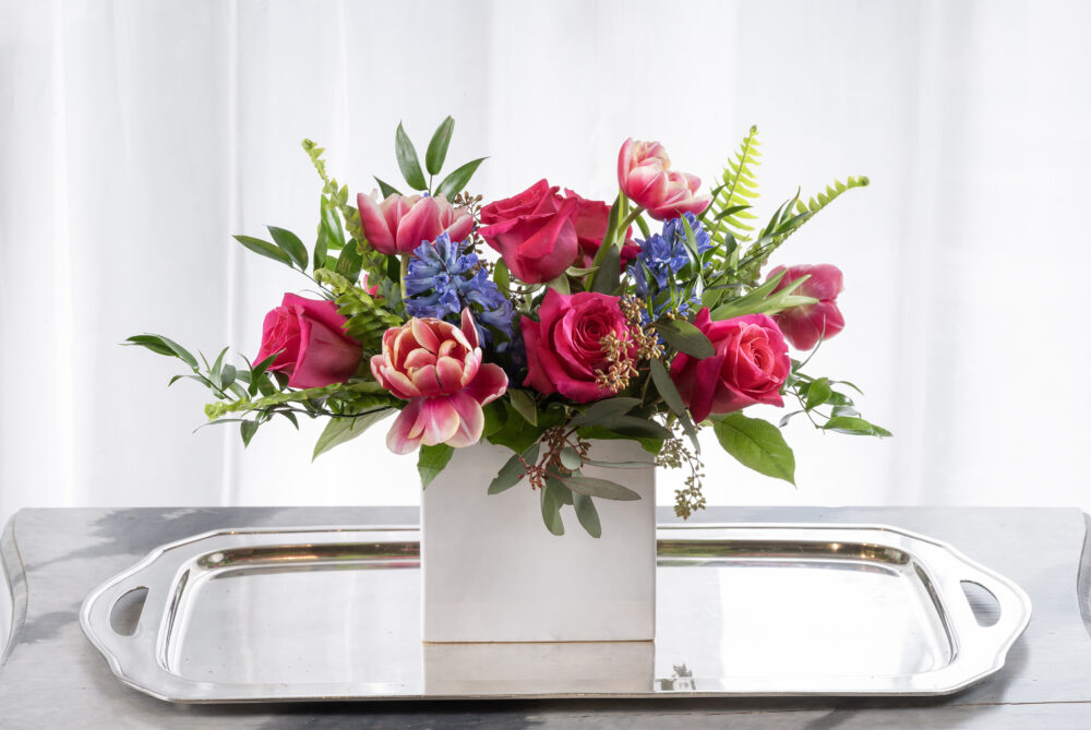 Gift a vibrant Valentine of pink roses and spring tulips with periwinkle hyacinth flowers in a slim white rectangle.