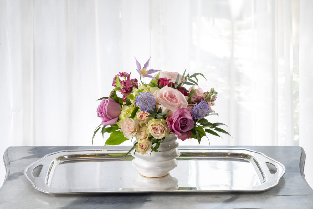 Colorful blossoms in a cheerful fresh flower arrangement, designed in a handmade white ceramic pot.