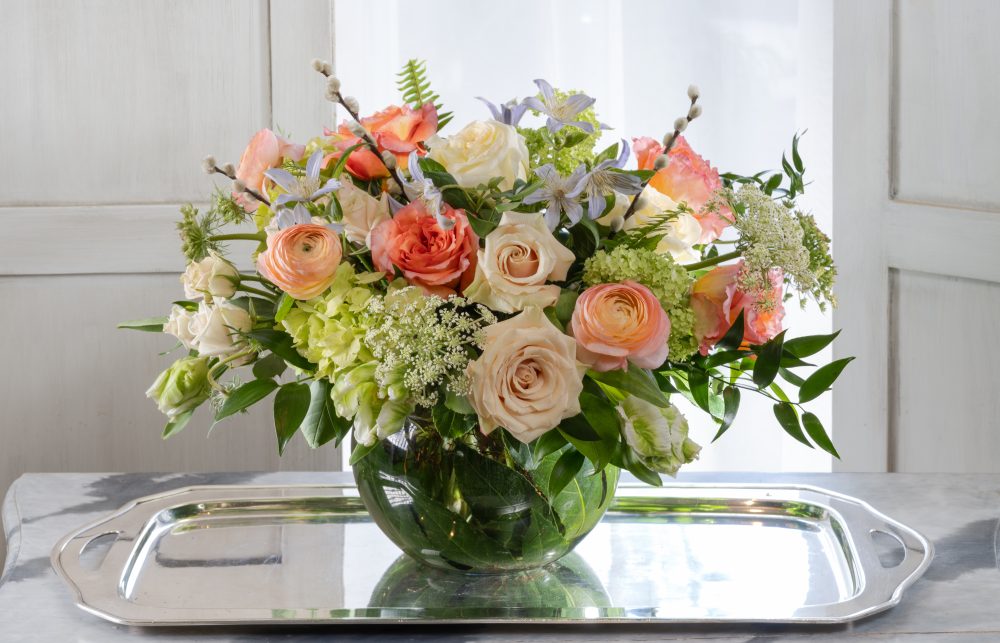Bright pastel fresh flowers with blush, peach, and coral blossoms in an emerald leaf wrap, delivered.