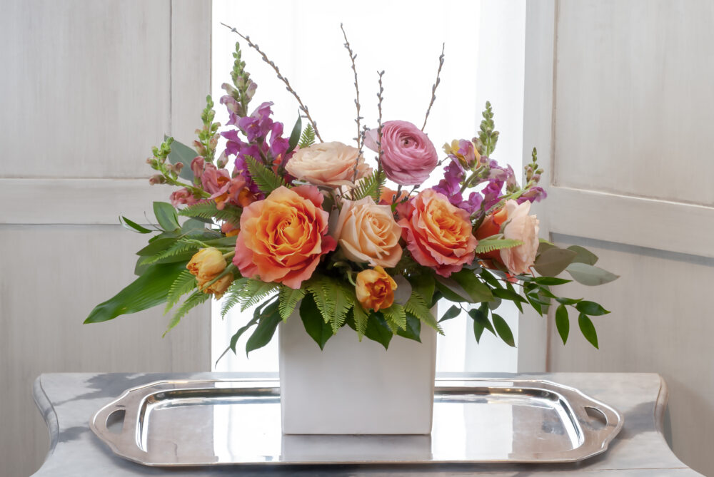 Bright and beautiful fresh flowers with peach, pink, and coral arranged in a matte white slim rectangle.