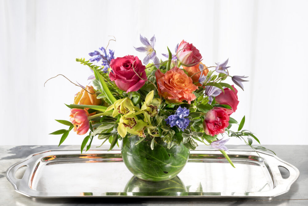 Vibrant spring fresh flower arrangement with bold pink, coral, and purple blossoms accented with pretty green orchids.