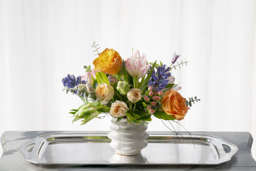 Bright spring colors with Dutch tulips and roses in a playful white ceramic pot.