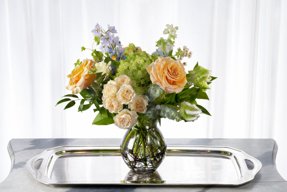 Soft and sweet seasonal fresh flower arrangement with peach and blue in a bouquet vase.