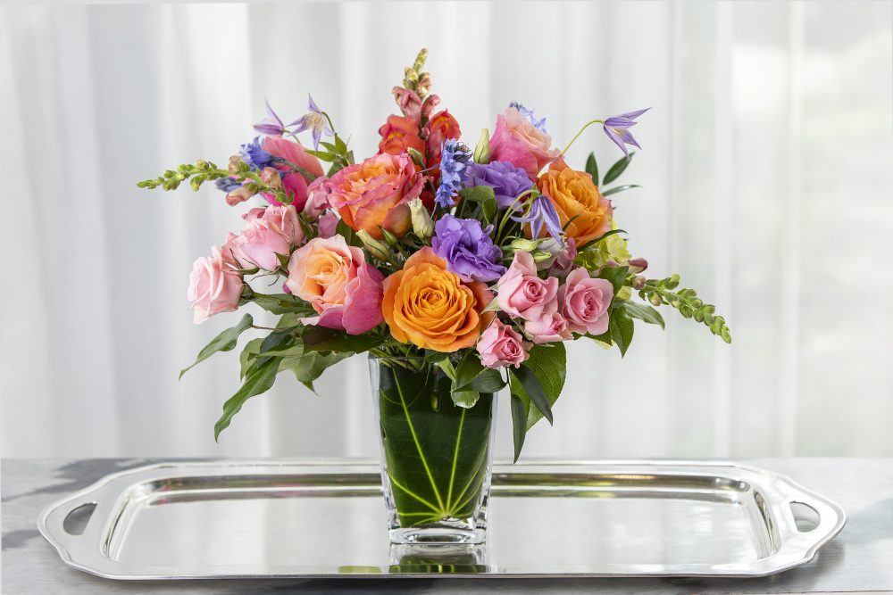 Bright beauties in coral, pink, and lavender in a bouquet-style, arranged in an emerald leaf wrap for a pretty Mother’s Day gift, delivered.