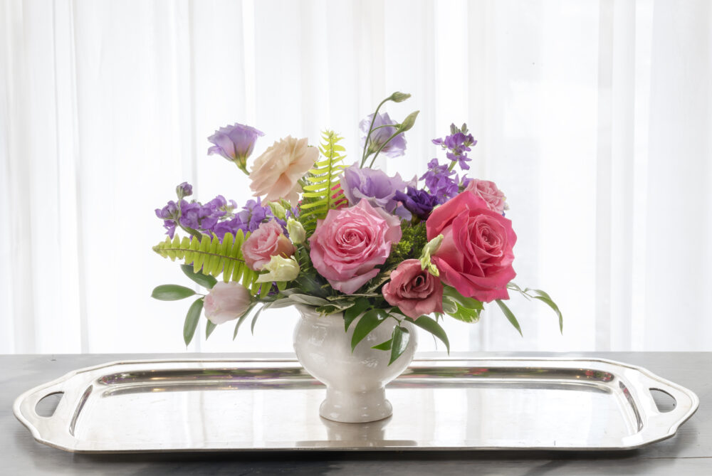 Cheerful and sweet fresh flower arrangement in vibrant pink and purple blooms designed in a pedestal vase for a charming Mother’s Day gift.