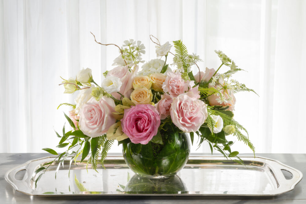 Fresh flowers with beautiful roses in pretty pinks, peaches, and whites wrapped in an emerald leaf-lined cylinder, delivered.