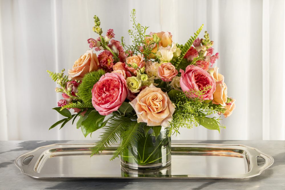 A delightful bright mix of summer fresh flowers with coral, peach, and green in an emerald leaf wrap for a cheerful gift, delivered.