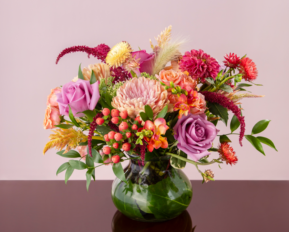 A soft autumn seasonal mix of fresh flowers with purple, mauve, peach, lavender and wine red blossoms in a glass posey vase, delivered.