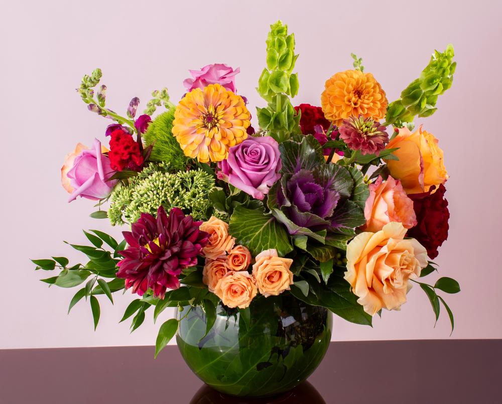 A vibrant purple peach mix of autumn fresh flowers with purple, peach, coral, and magenta blossoms in a glass rose bowl, delivered.