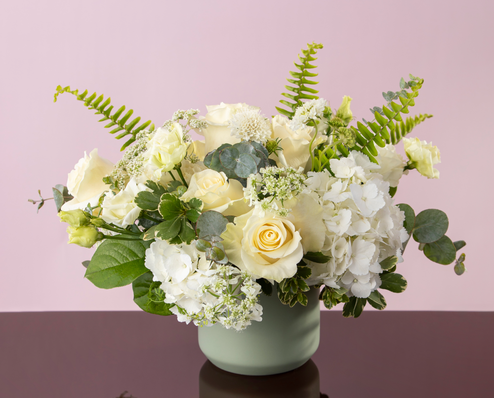 A fresh white and green mix of autumn seasonal flowers in a pastel green ceramic cylinder vase, delivered