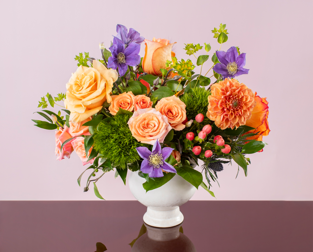 A fresh peach, coral and lavender mix of autumn seasonal flowers in a cream ceramic compote vase, delivered
