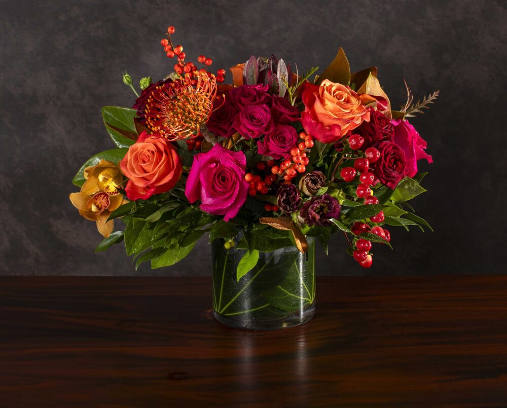 A bright pink and orange mix of autumn fresh flowers with pink, orange, red and burgundy blossoms in a glass cylinder vase, delivered.