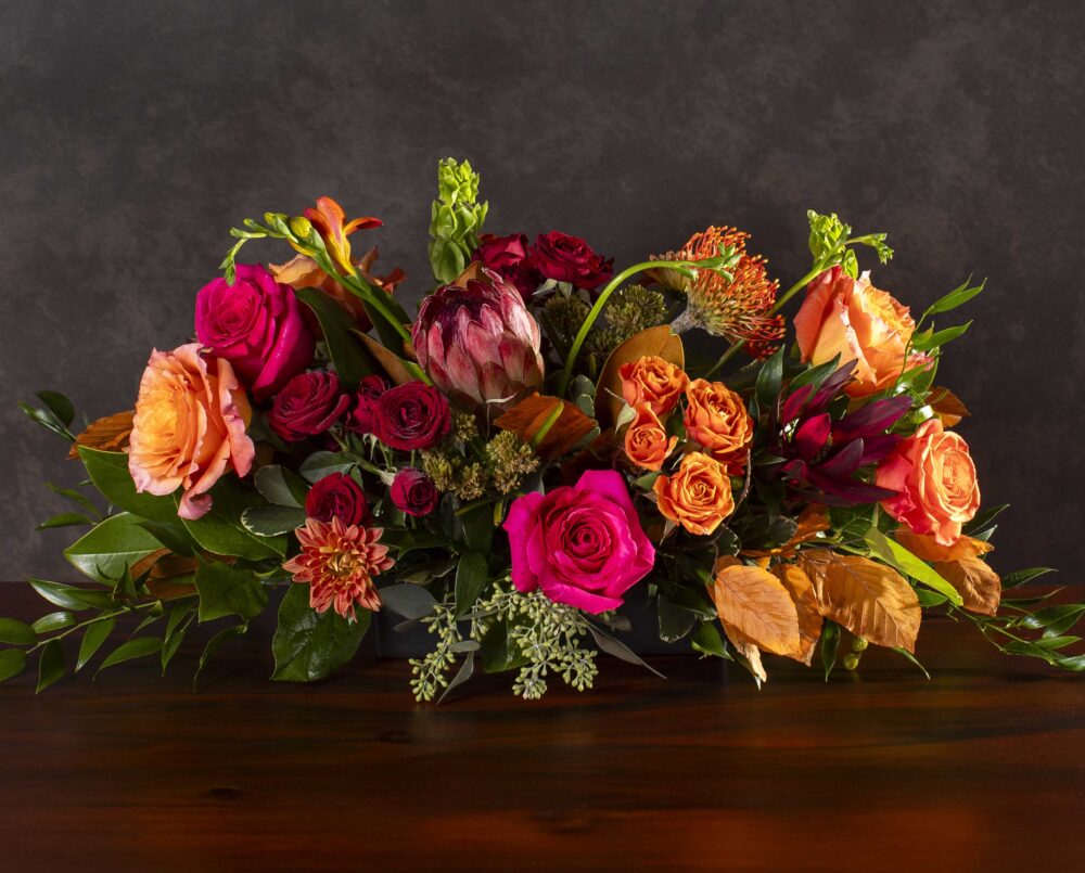 A fresh, bright mix of bright pink, orange and burgundy autumn seasonal flowers in a glass vase, delivered, thanksgiving