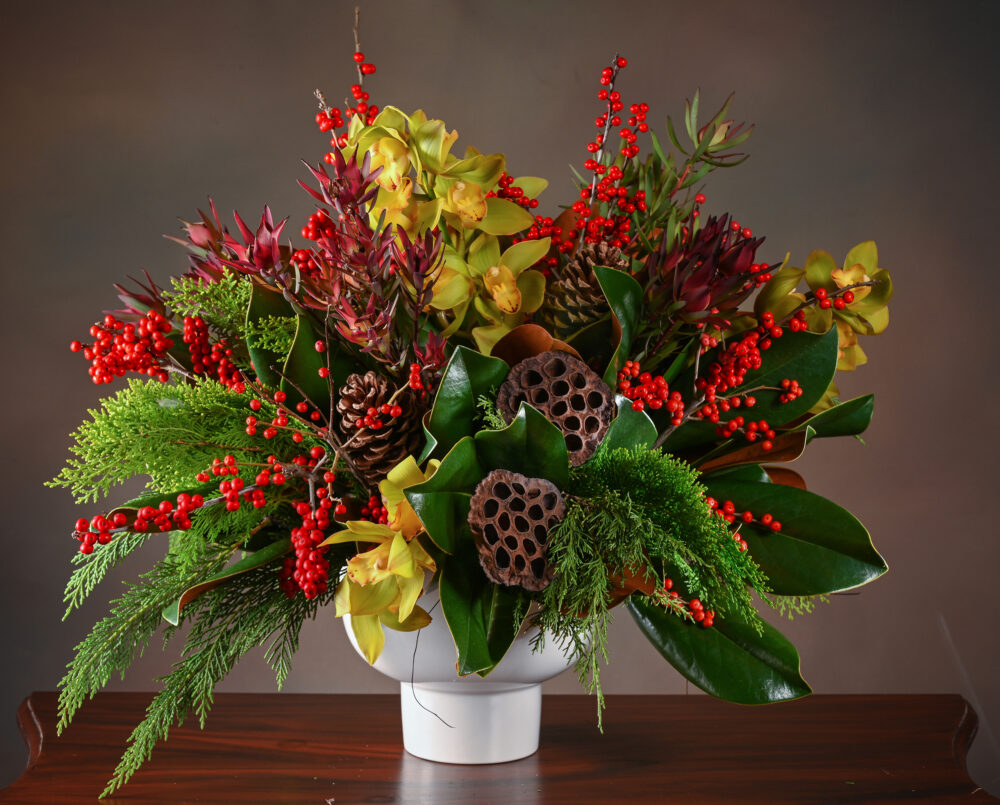 Large, creative, flower arrangement, green orchids, red berries, brown pods, evergreen, magnolia in a white ceramic pedestal vase, delivered, holiday, Christmas