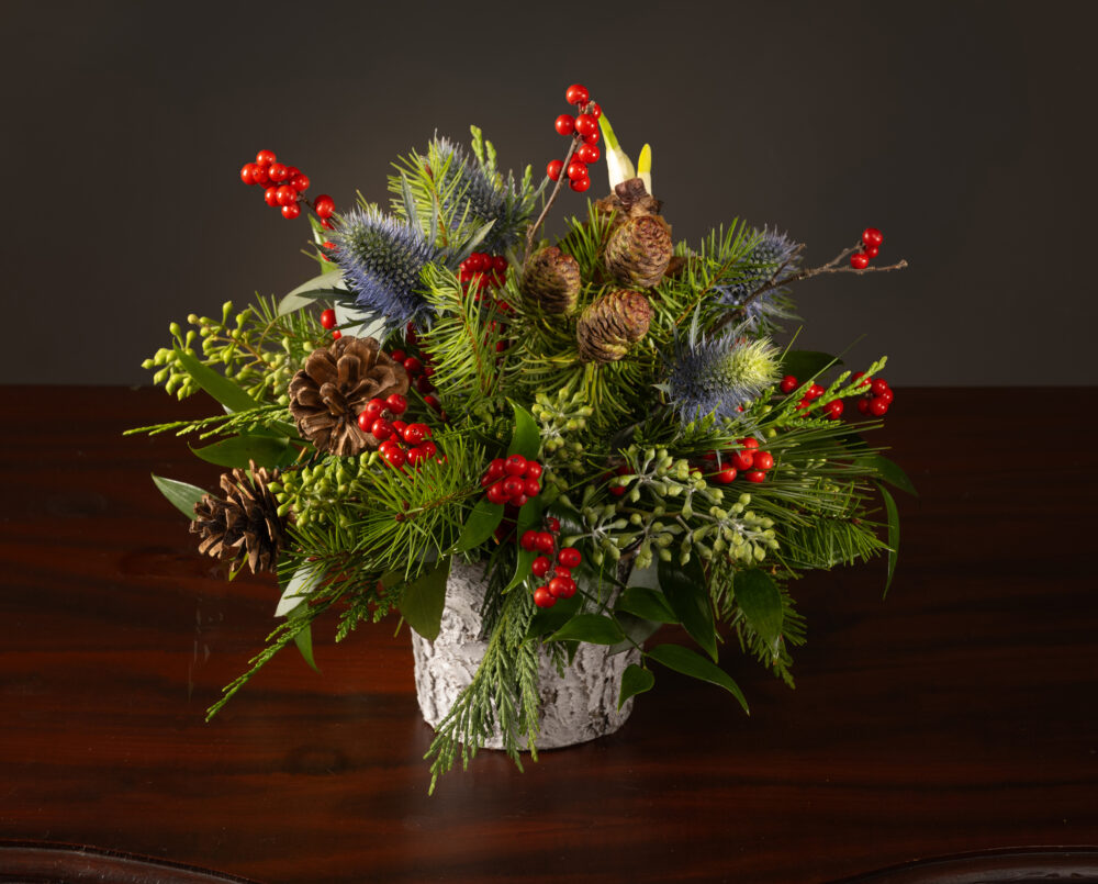 Petite holiday arrangement with seasonal texture, blue eryngium, red ilex berries, pinecones and bulbs in a white birch vase, delivered, holiday, Christmas.
