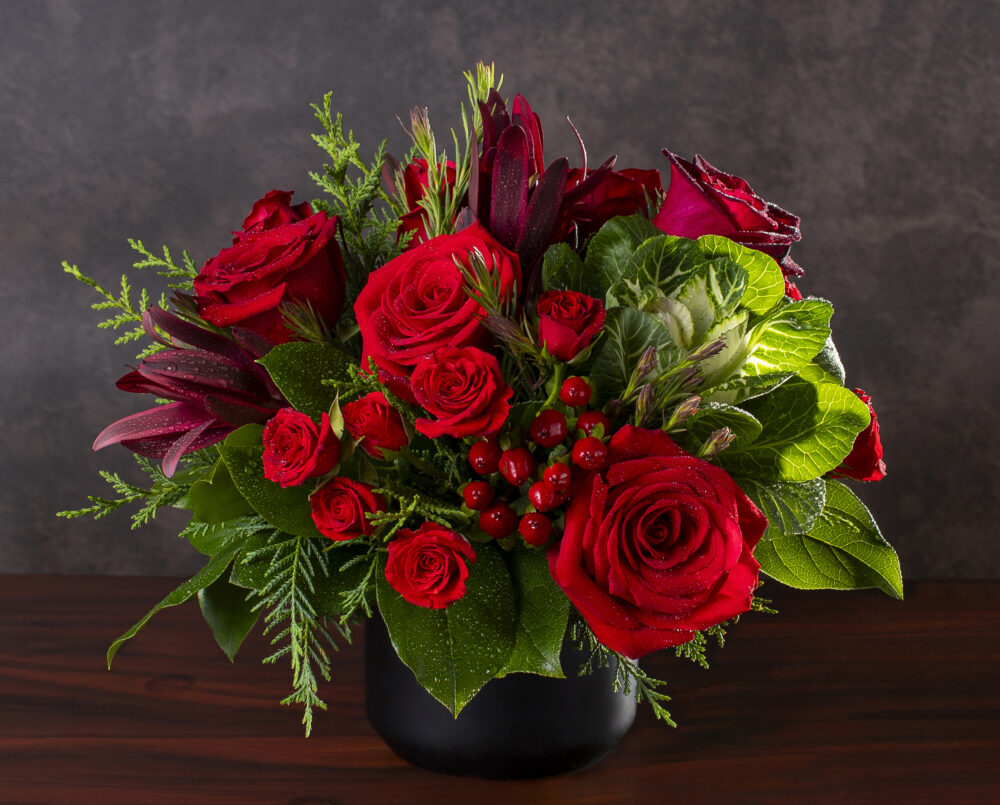 A unique red, green, holiday, flower arrangement in a ceramic vase with evergreen, kale, rose, hypericum, delivered, holiday, christmas