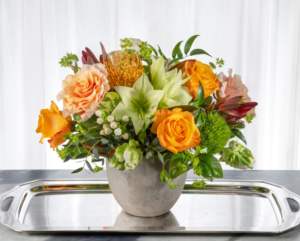 A bright mix of winter florals in shades of peach, green, orange, white, in concrete pot, delivered, winter.
