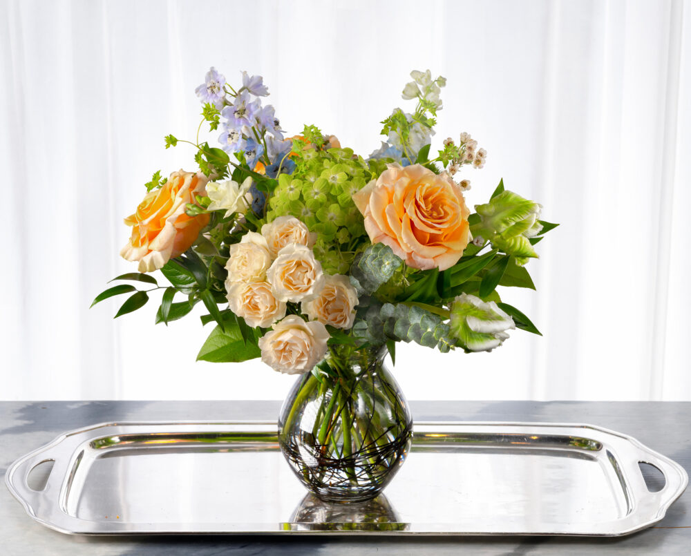 Seasonal winter flower arrangement including roses, tulips, hydrangea, delphinium in peach, green and blue in a glass vase, delivered.