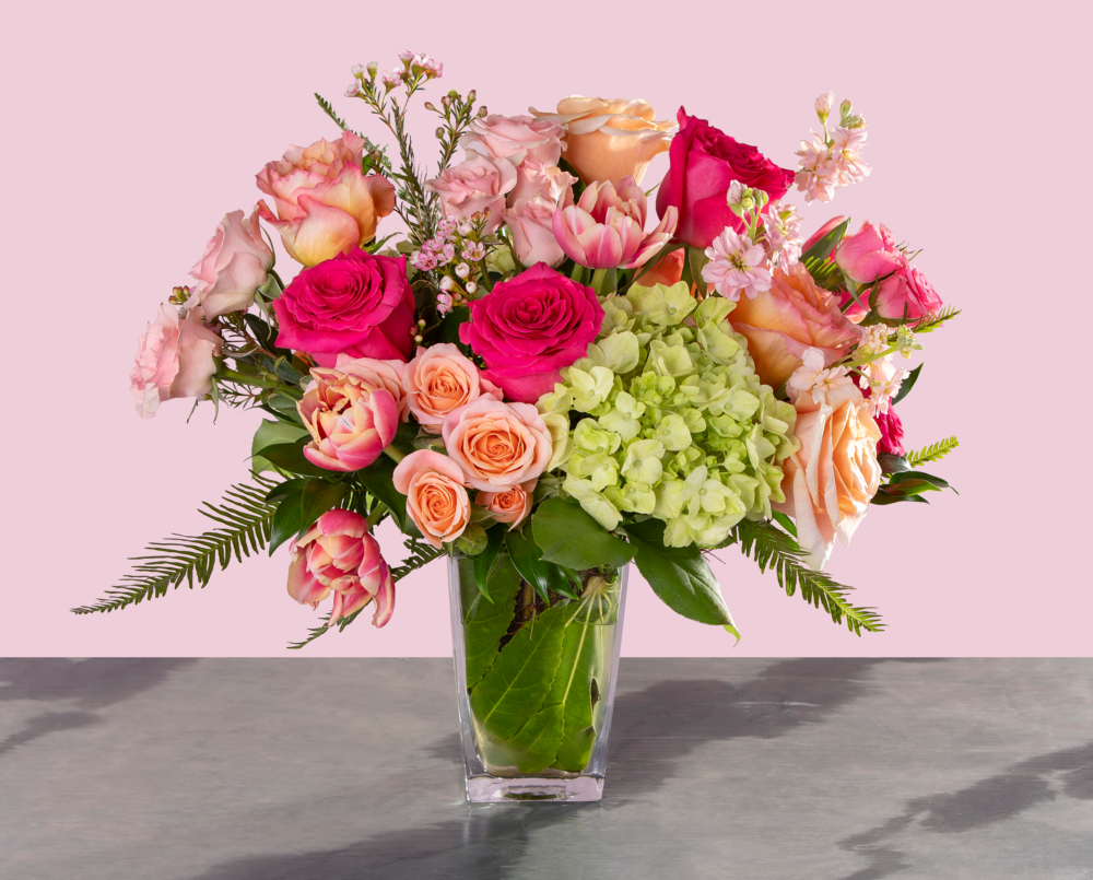 Georgie is a bright pink, peach and green Valentine arrangement in a tall glass vase with a leaf wrap.