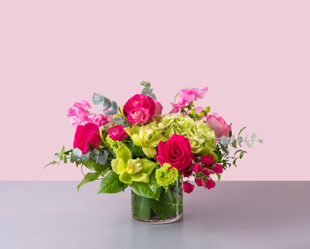 Cerise is a bright pink and green arrangement with orchids, ranunculus and roses in a glass cylinder vase.