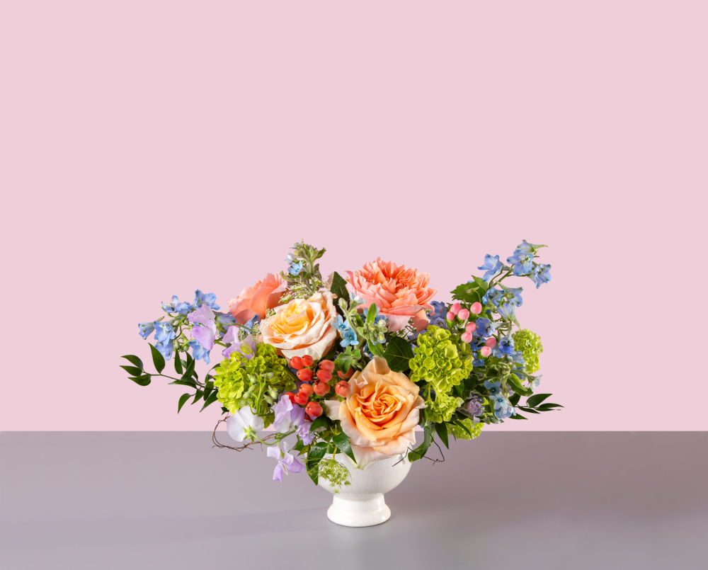 Felicity is a petite arrangement with garden roses, sweet peas, hydrangea, delphinium in a ceramic compote vase.