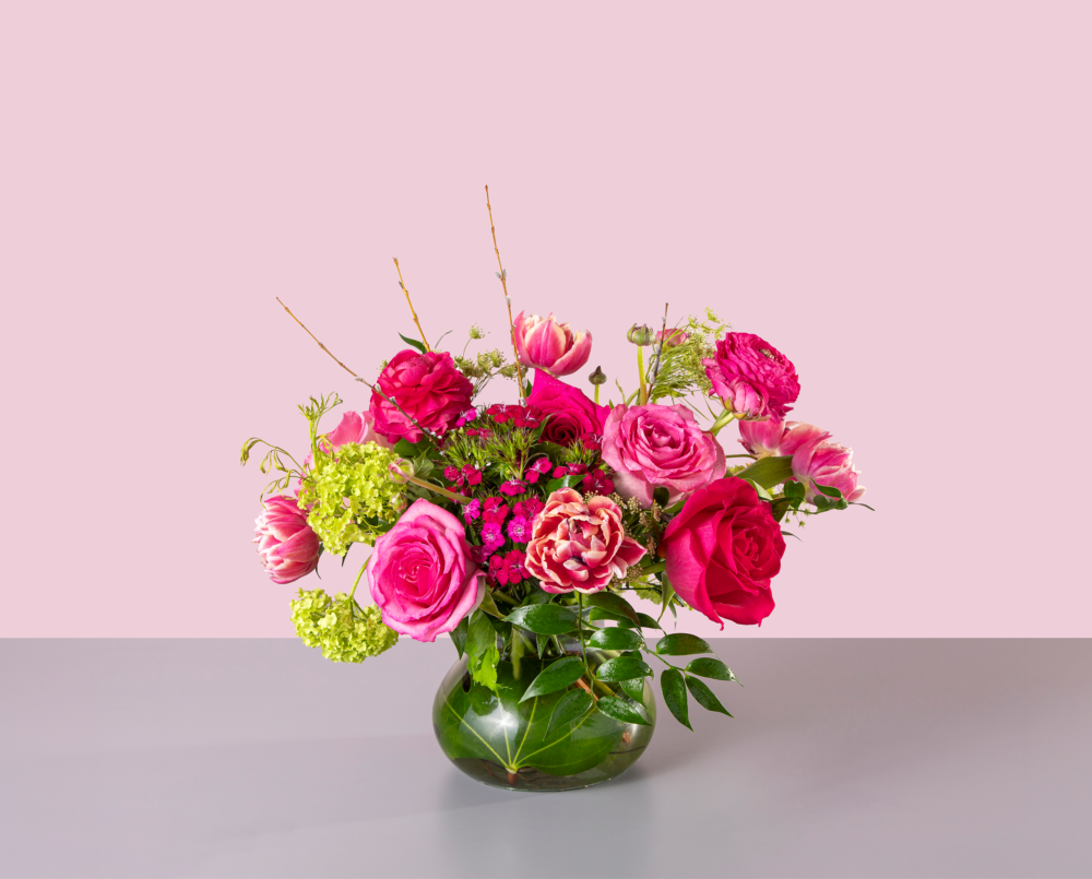 Hazel is a vibrant pink and green arrangement with roses, ranunculus and viburnum in a glass Posie vase.