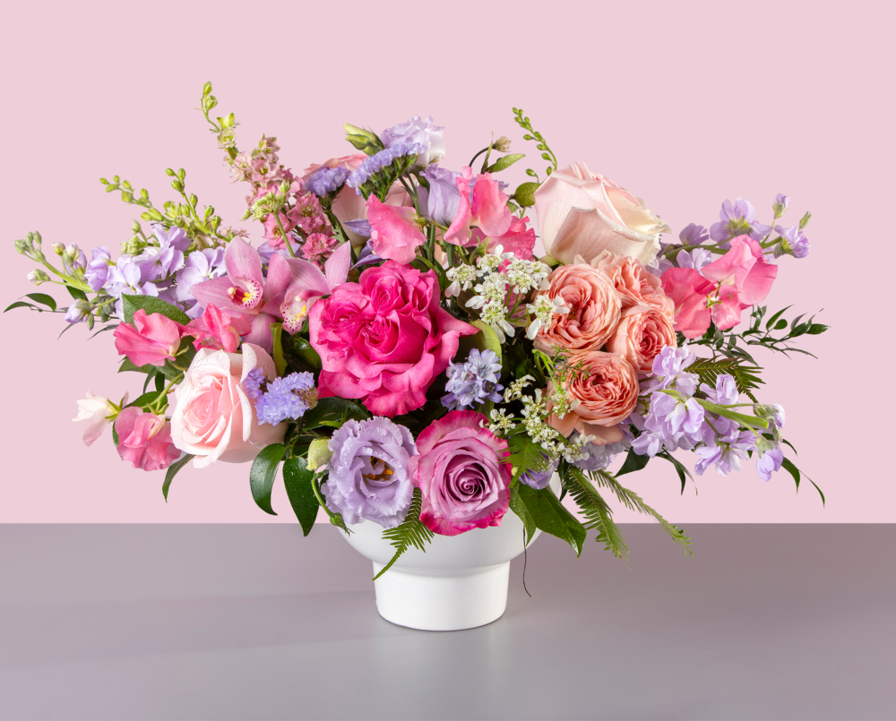 Imogen is a large bright pastel arrangement of roses, orchids, sweet peas in a ceramic compote vase.
