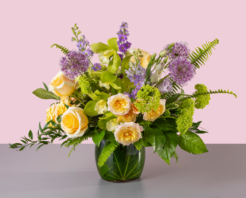 Paloma is a large arrangement in shades of lavender, yellow and green in a glass vase with a leaf wrap.