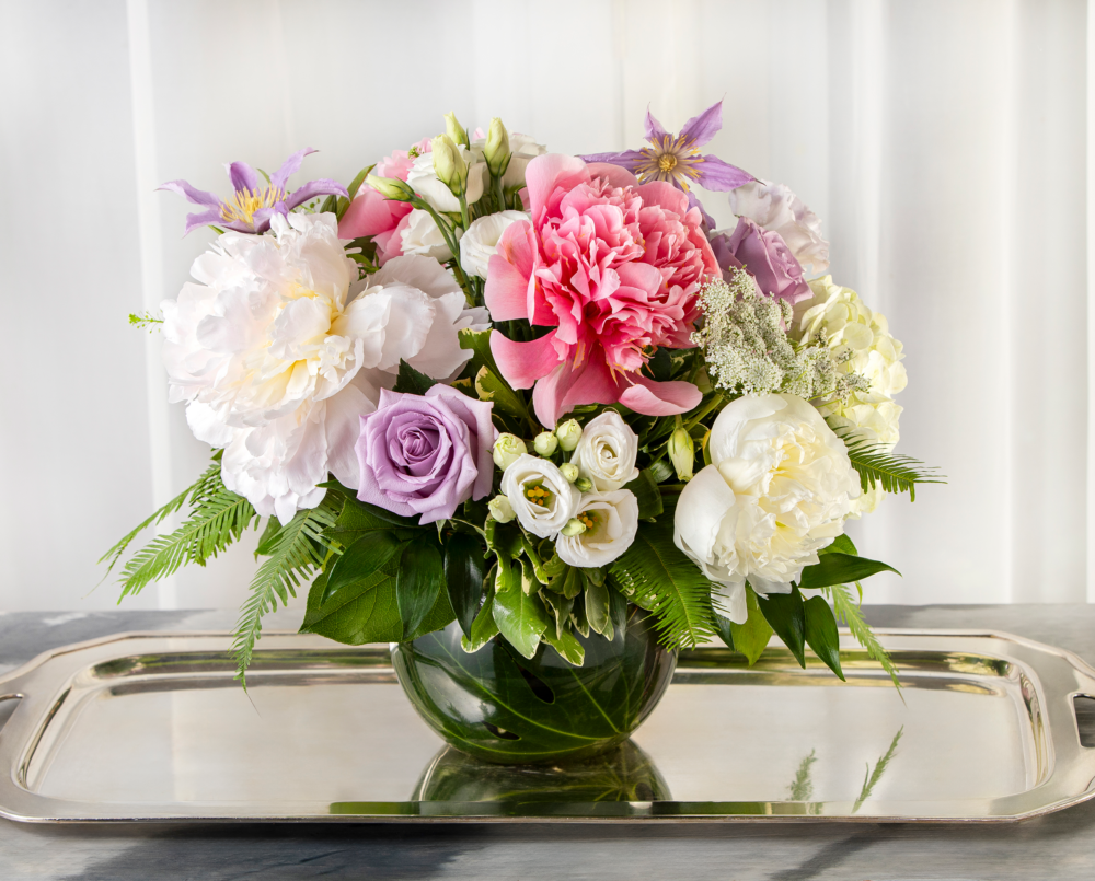 Sylvie is a white, pink and lavender arrangement with peonies and clematis in a clear glass vase.