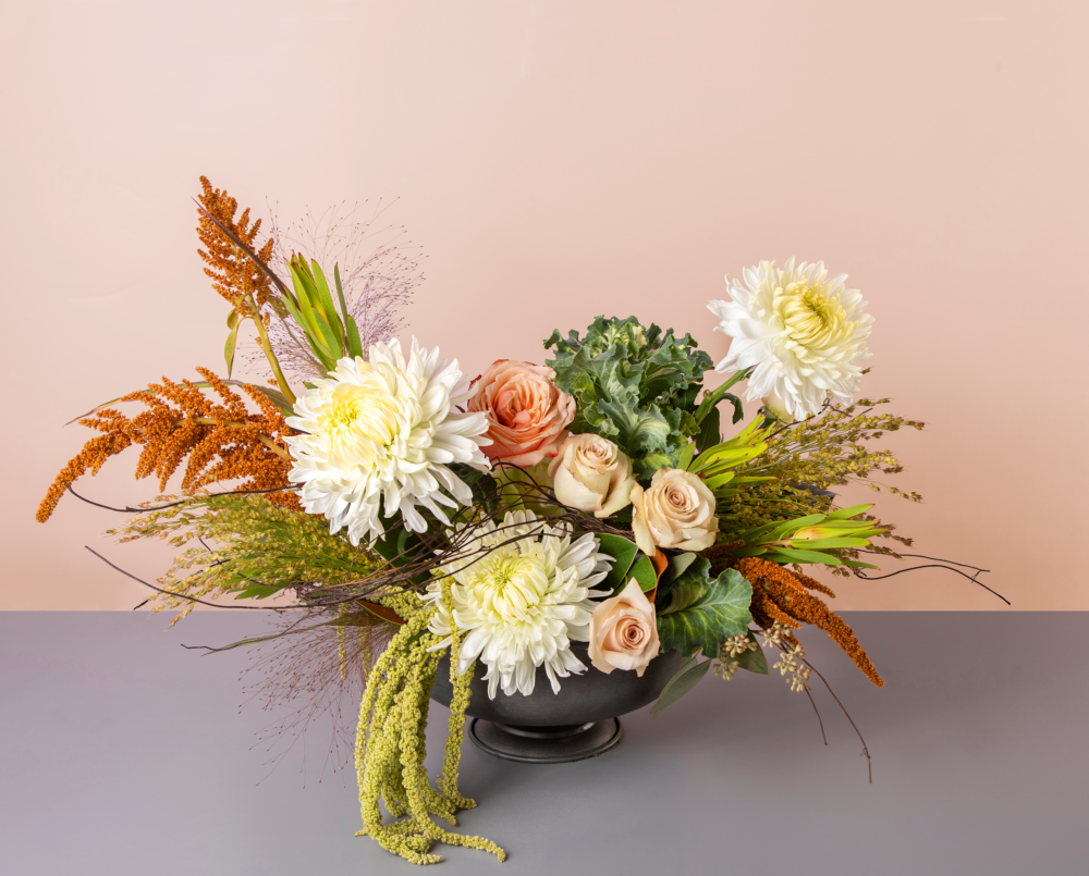 Dolly is a asymmetrical arrangement in shades of brown, blush, white and green in a black compote vase.