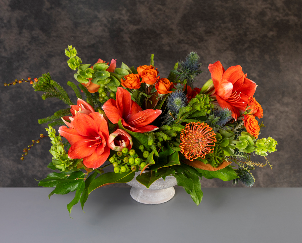 Aviva is a bright autumn arrangement with orange amaryllis in a stone pedestal vase.
