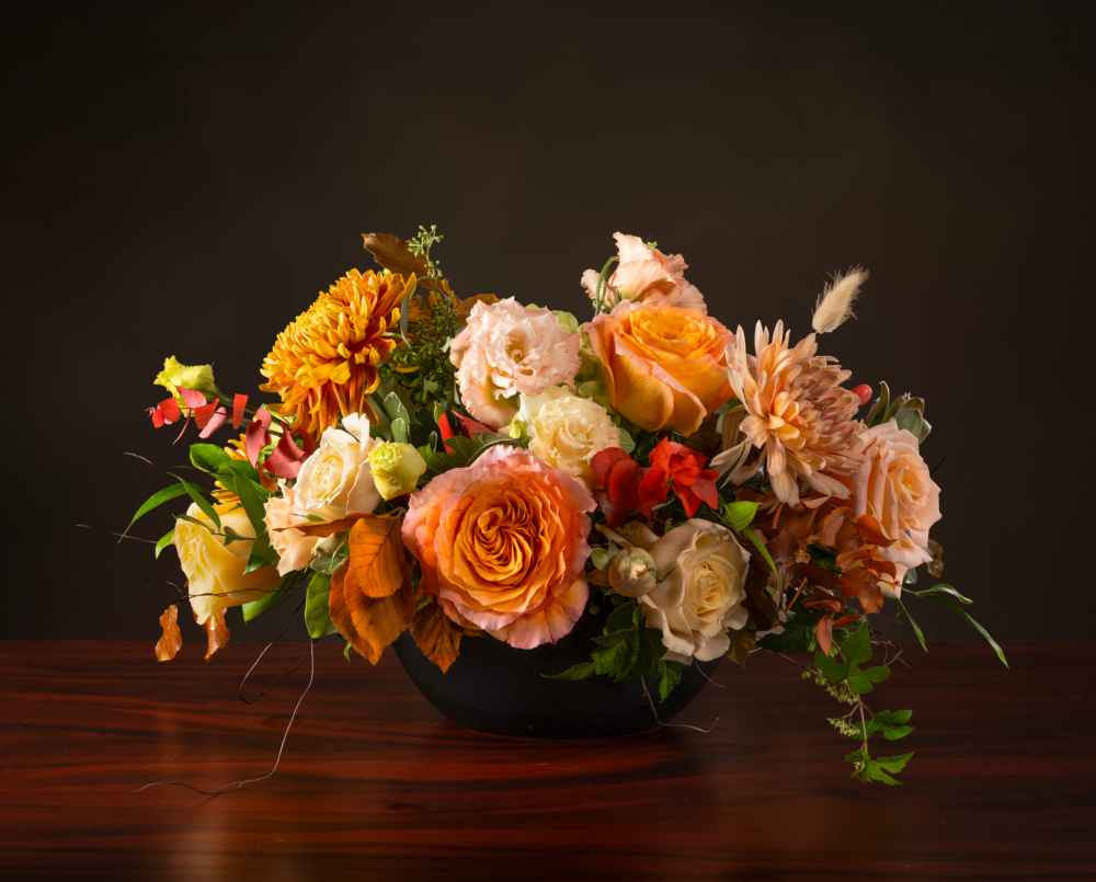 Colette is an oval shaped flower arrangement in shades of peach, blush and white in a black ceramic oval vase.